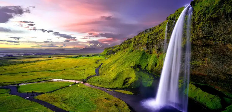 A waterfall over a green landscape in the evening