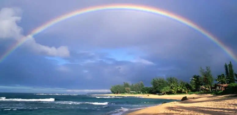 A rainbow stretching between the ocean and the beach